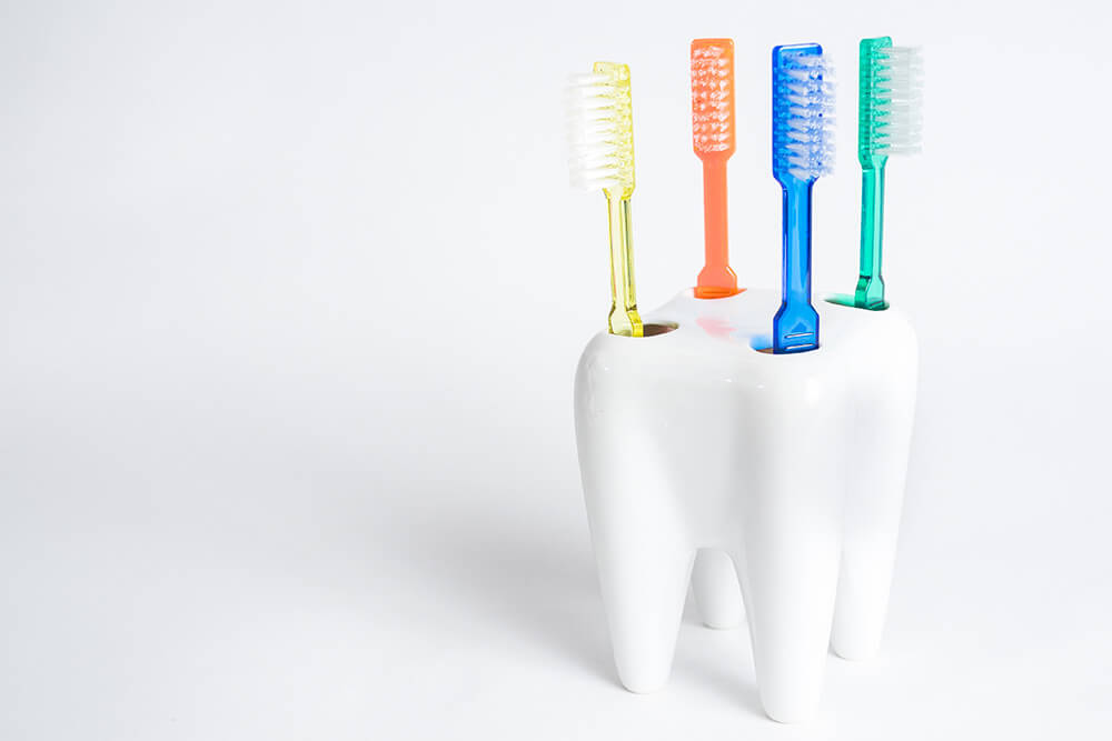 Ein Zahnbürstenhalter in Form eines Zahnes ist mit vier farbigen Zahnbürsten bestückt.
