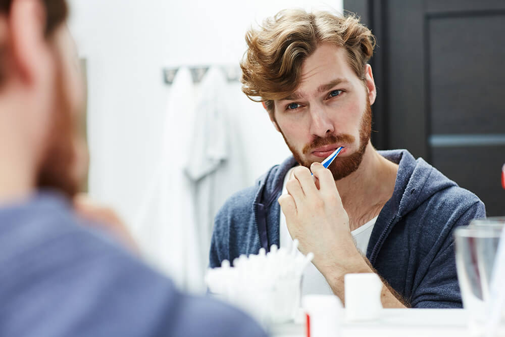 Ein Mann steht vor dem Spiegel und putzt sich die Zähne.