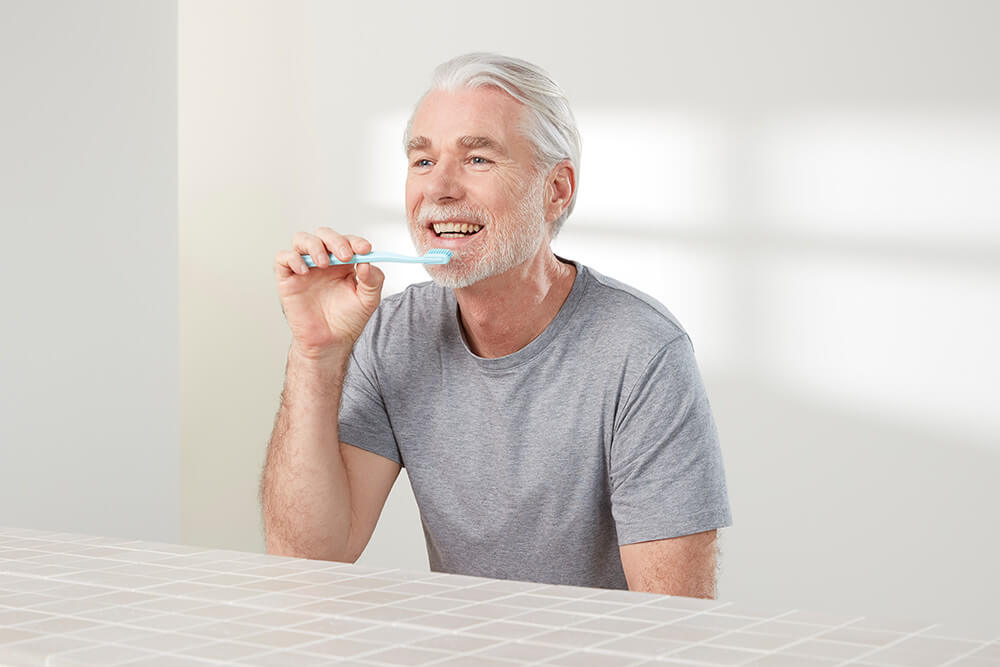 Ein älterer Mann putzt sich freudestrahlend seine gesunden Zähne.